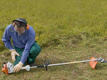 : Step 7 of 14: Secure footing / pushing the brushcutter onto the ground Make sure you have a secure footing and check once again that the brushcutter is lying in a secure position. Push the machine firmly down onto the ground so that it cannot tilt when starting. Check that the cutting attachment is not touching anything.