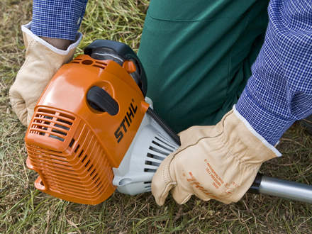 : Step 7 of 14: Secure footing / pushing the brushcutter onto the ground Make sure you have a secure footing and check once again that the brushcutter is lying in a secure position. Push the machine down onto the ground so that it cannot tilt when starting. Check that the cutting attachment is not touching anything.